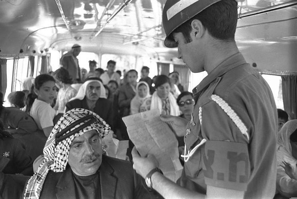 An Israeli military police officer checks entry permits of Palestinians on a bus crossing the Allenby Bridge into Israel. (Moshe Milner/GPO)