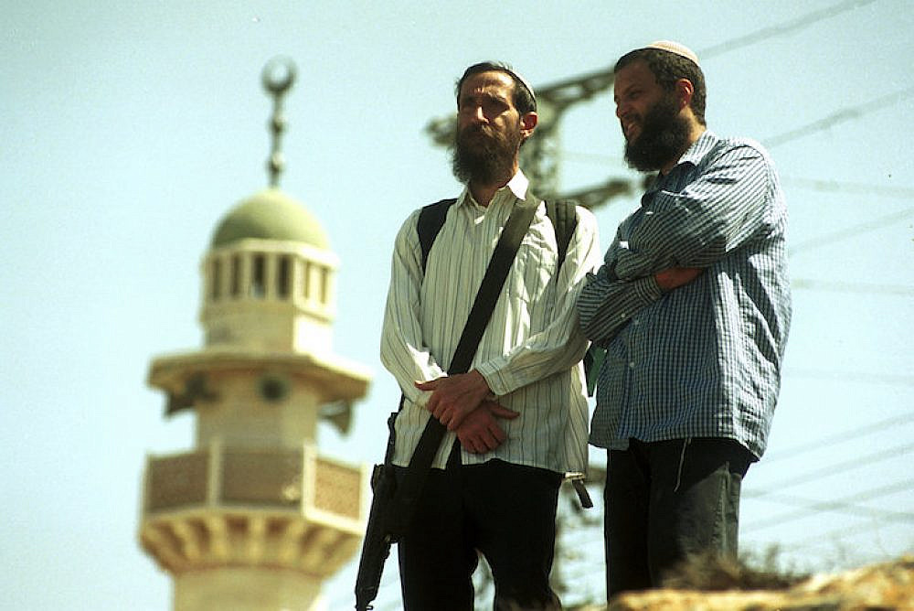 Two settlers, one of them carrying a gun, stand near a mosque in the West Bank city of Hebron, April 1, 2001. (Nati Shohat/Flash90)