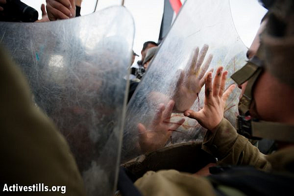 Palestinians press their hands against riot shields held by Israeli soldiers during a weekly demonstration against the occupation and separation wall in the West Bank village of Al Ma'sara, December 14, 2012. The Israeli separation wall, if built as planned, would cut off the village from its agricultural lands. (photo by: Ryan Rodrick Beiler/Activestills.org)