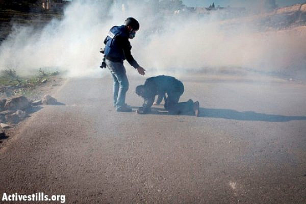 A press photographer helps his colleague which was hit from a tear gas canister shot by Israeli soldiers, during a protest against the occupation in the West Bank village of Nabi Saleh, December 23, 2011  (Photo by: Oren Ziv/ Activestills.org)