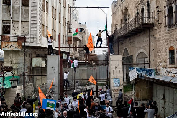 During a  protest against the continued closure of Shuhada Street to Palestinians, demonstrators climb a fence, bulit by the Israeli army in the West Bank city of Hebron February 22, 2013. Hundreds of demonstrators, including foreign and Israeli activists, gathered to mark the 19th anniversary of the closure of the street by the Israeli army in 1994 following the massacre by Baruch Goldstein, an Israeli settler, who went on a rampage inside Al Ibrahimi Mosque, killing 29 Palestinian worshipers.  (Photo by: Oren Ziv/Activestills.org)