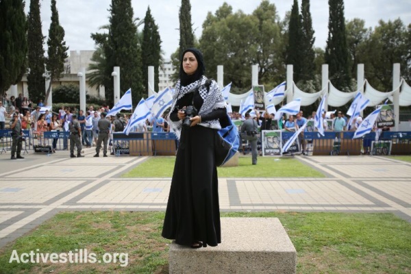 A Palestinian photographer standing during a minute of silence commemorating the Nakba, during a ceremony held by Palestinian and Israeli students in the entrance to the Tel Aviv University. Rightwing vigil protesting the ceremony and policemen are seen in the background. May 13, 2013 (photo: Yotam Ronen / Activestills)