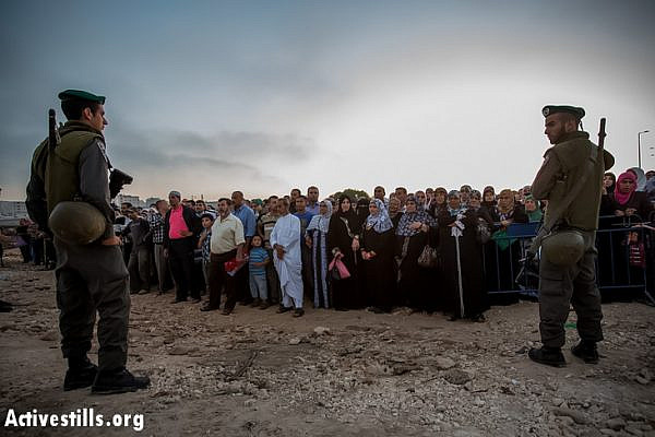 Border police officers stand in front of Palestinians as they wait to cross from Qalandiya checkpoint outside Ramallah, West Bank, into Jerusalem to attend the second Friday Ramadan prayers in the Al-Aqsa Mosque, July 26, 2013. (Photo: Activestills.org)
