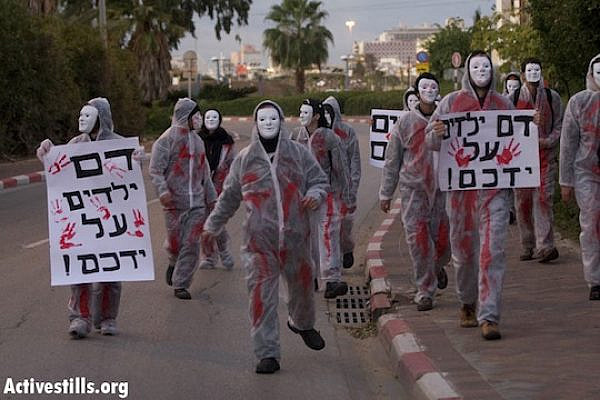 Protesters in white suits covered in fake blood arrive at Sde Dov Air Force Base in north Tel Aviv to protest Operation Cast Lead, January 2, 2013. The signs read: "You have children's blood on your hands." (Photo: Activestills.org)