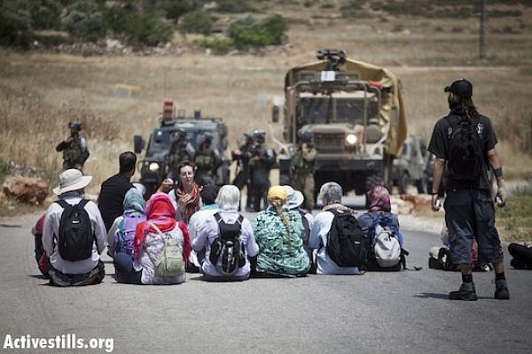 Demonstrators sit in front of the "Skunk" water canon, during the weekly protest against the occupation in the West Bank village of Nabi Saleh, May 18, 2012. (Photo by: Oren Ziv/ Activestills.org)