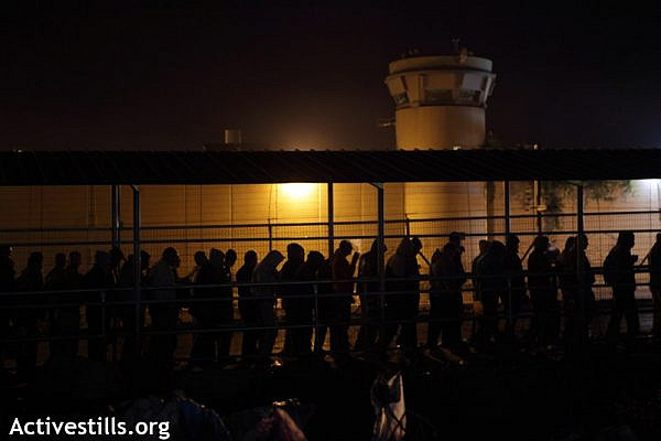 Palestinians workers walk next to the Wall and an Israeli military tower to cross very early the Eyal Israeli military checkpoint into Israel in order to reach their workplace, Qalqiliya, West Bank, 22.11.2011. Thousands of Palestinians are passing this checkpoint every morning, some coming as early as 4am. (Photo by: Anne Paq/Activestills.org)