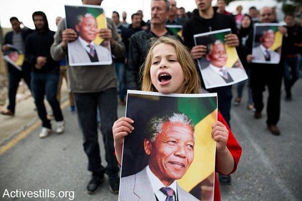 A protester holding a poster with Nelson Mandela's portrait, during a demonstration in the West Bank village of Nabi Saleh, December 7, 2013. The demonstration marked four years to the Popular Struggle in Nabi Saleh, while commemorating the killing of Mustafa Tamimi and Rushdi Tamimi by Israeli army forces, and twenty six years since the first Intifada.