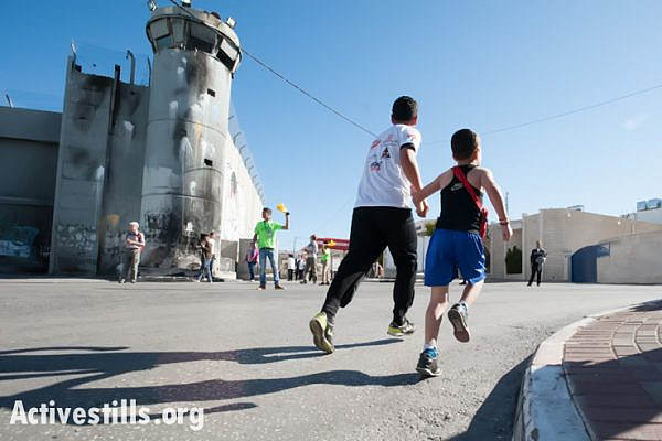 A Palestinian father and son run past the Israeli separation wall dividing the West Bank town of Bethlehem during the second annual Palestine Marathon, April 11, 2014. (photo: Activestills.org)