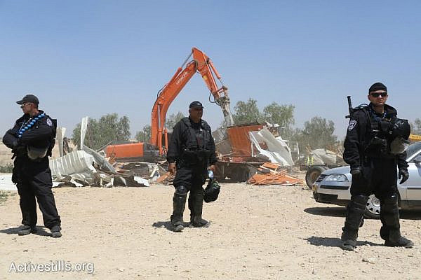 Israeli policemen stand by as a bulldozer demolishes the Bedouin village of Al-Arakib for the 64th time (photo: Activestills.org)