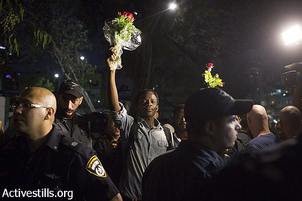 African asylum seekers hold flowers as residents of south Tel Aviv and right-wing activists protest against the Israeli High Court decision to cancel the "infiltrator law" and close the Holot detention center, South Tel Aviv, October 5, 2014. (Activestills)