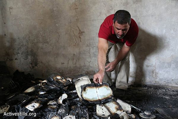 A man inspects Qurans damaged in a suspected arson hate crime against a mosque in the West Bank village of Al Mughayir, November 12, 2014. (Photo by Oren Ziv/Activestills.org)