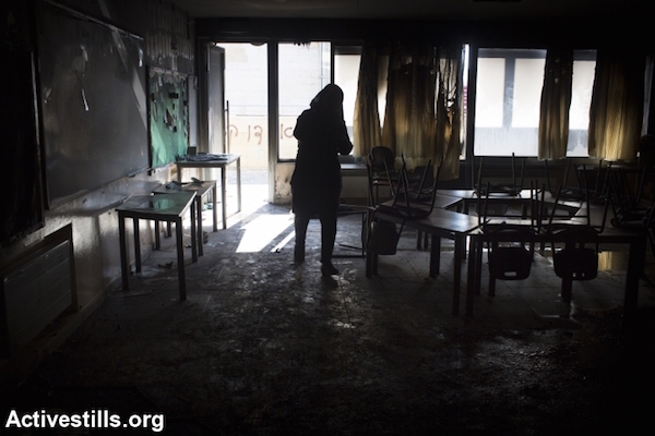 A teacher inspects the damage from an arson attack that targeted first-grade classrooms at a Jewish-Arab school near the Palestinian neighborhood of Beit Safafa in southern Jerusalem, November 30, 2014. Spray painted on the walls were racist slogans in Hebrew reading: "Death to Arabs" and "There's no coexistence with cancer". (Photo by Oren Ziv/Activestills.org)