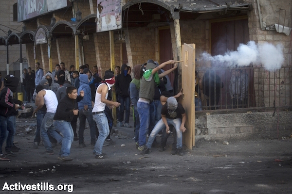 Palestinian youth take cover behind a door as they shoot fireworks toward Israeli Border Police during clashes at a checkpoint between the Shuafat refugee camp and the rest of Jerusalem, November 6, 2014. (Photo by Oren Ziv/Activestills.org)