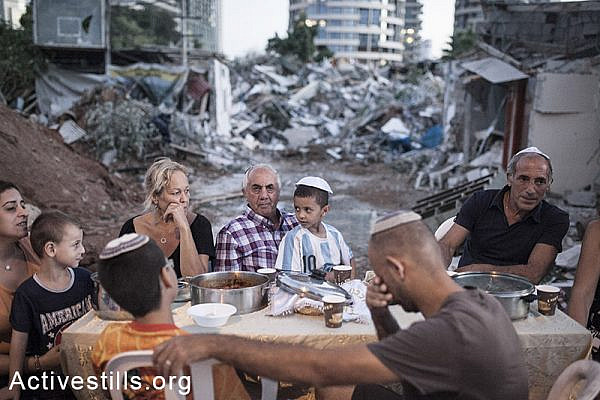 The Kadoori, Hamias, and Ashram families sit at an improvised Shabbat dinner table next to their demolished houses in Givat Amal, Tel Aviv, Sep. 19, 2014. (Shiraz Grinbaum/Activestills.org)