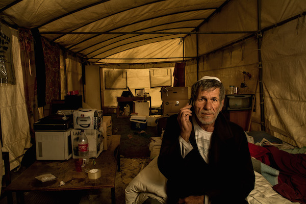 A man sits in his tent at the Arlozorov encampment in Tel Aviv. (Photo by Dan Haimovich)