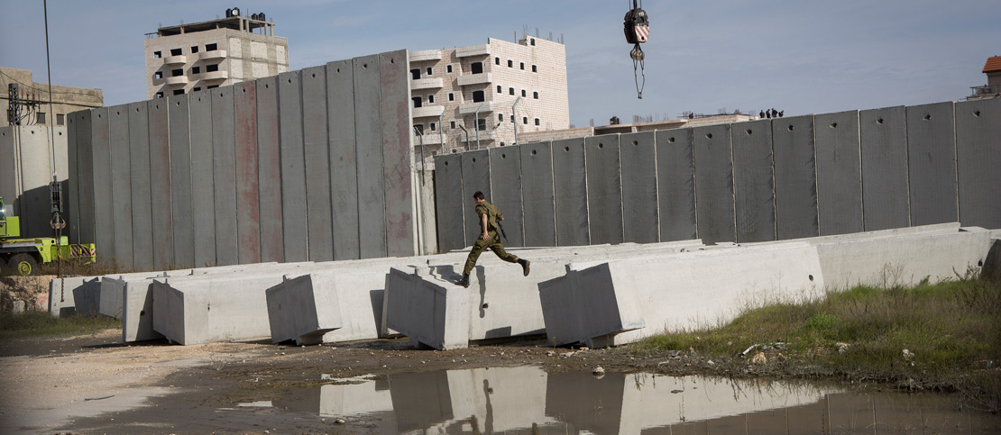 An Israeli soldiers is seen jumping along concrete blocks as Israeli authorities install a new section of the separation wall surrounding the Shuafat Refugee Camp in East Jerusalem, December 3, 2014. (Activestills.org)