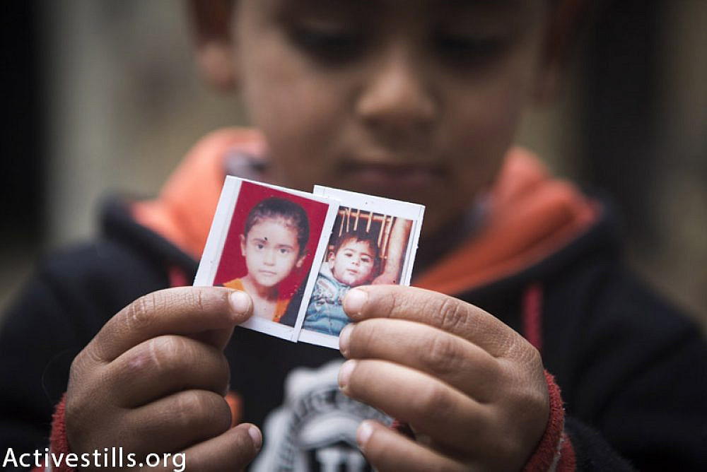 Fadi Ibrahim Abu Khusa (4) holds the photo of his two killed siblings, Shahed (9) and Mohammed (2), in their home in Zawaida village, central Gaza Strip, February 24, 2015.  The two children were killed with their parents, Ibrahim and Sabreen, and 4 other members of their family by an Israeli attack on their home which occured on July, 30, 2014. Ibrahim and Sabreen went to the home of Sabreen's father one week before the attack thinking they would be safer. (Anne Paq / Activestills.org)