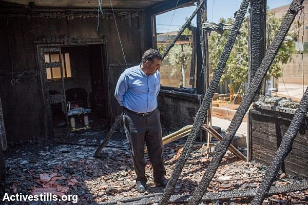 A man examines the burnt house of the Dawabsha family during the funeral procession of Saad Dawabsha, in the West Bank village of Duma, August 8, 2015. (photo: Yotam Ronen/Activestills.org)