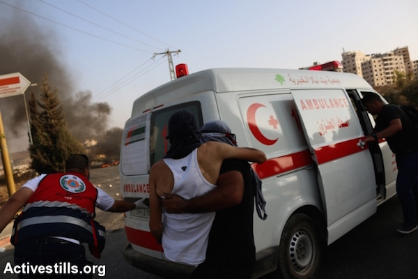 A Palestinian youth is carried to an ambulance during clashes at the DCO checkpoint in the West Bank, October 5, 2015 (Muhannad Saleem/Activestills)