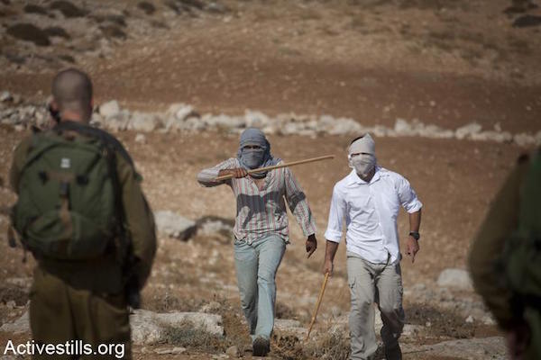 File photo of masked Israeli settlers threatening Palestinians while soldiers look on. (Oren Ziv/Activestills.org)