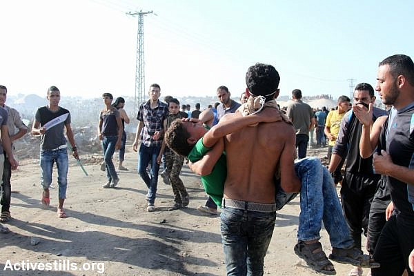 A Palestinian protester carries an injured child during a demonstration near the Gaza border, at the proximity of Nahal Oz crossing,  Northern Gaza Strip, October 16, 2015. Thousands of Palestinians marched towards the border in different locations in the Gaza Strip following a call for protests for a 'day of rage'. Two Palestinians were killed by the Israeli forces during the demonstrations. (photo: Ezz Zanoun/Activestills.org)
