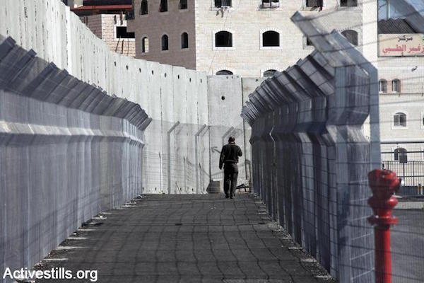 A Palestinian resident of East Jerusalem walks into a checkpoint that separates the entirely walled-off neighborhood of Shuafat Refugee Camp, East Jerusalem, December 27, 2011. (Anne Paq/Activestills.org)