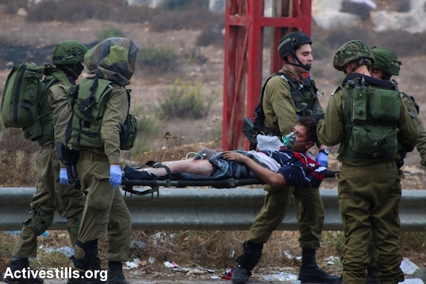 Israeli army medics carry away a young Palestinian stone thrower who was shot in the leg by undercover Israeli troops on the outskirts of Ramallah. A tourniquet can be seen on his leg where he was shot, October 7, 2015. (Muhannad Saleem/Activestills.org)