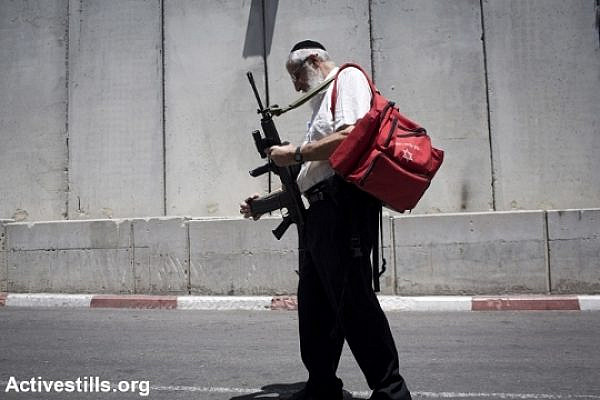 A religious Israeli man carries an M-16 rifle as he walks near the separation barrier surrounding Rachel's Tomb, Bethlehem, West Bank. (photo: Oren Ziv/Activestills.org)