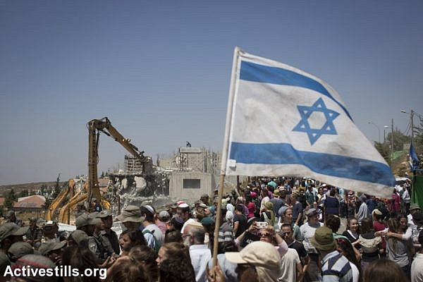 Israeli police forces stand guard while Israeli settlers watch on as bulldozers, under an Israeli High Court ruling, start the demolition of the so-called Dreinoff buildings in the settlement of Beit El, north of Ramallah in the West Bank, July 29, 2015. (photo: Oren Ziv/Activestills.org)