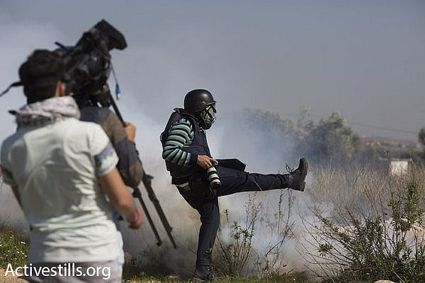 A press photographer kicks away a tear gas canister that Israeli troops fired toward a group of journalists, Bil’in, February 19, 2016. (Oren Ziv/Activestills.org)
