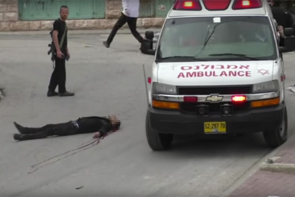 A Magen David Adom ambulance attempts to navigate around the body of a Palestinian man who shot in the head by an Israeli soldier in the occupied city of Hebron. The man, who reportedly took part in stabbing another soldier, had already been shot and incapacitated. March 24, 2016. (Screenshot/B’Tselem)