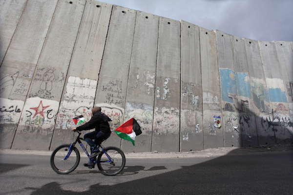 A Palestinian youth rides a bicycle adorned with Palestinian flags past the Israeli separation wall near Jerusalem. (Issam Rimawi/Flash90)