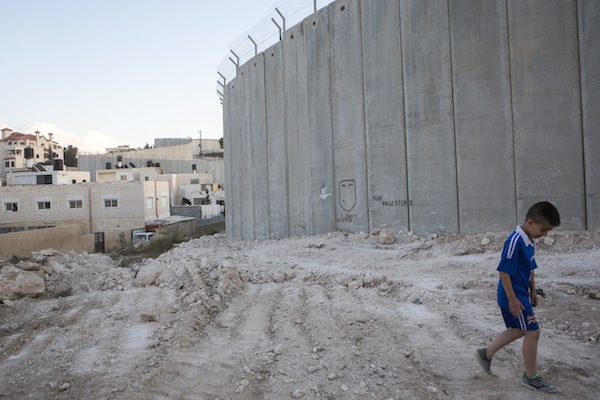 A young Palestinian boy walks by a section of the Palestinian side of the Separation Wall in the Jerusalem neighborhood of Abu Dis. September 29, 2014. (Photo by Miriam Alster/Flash90)