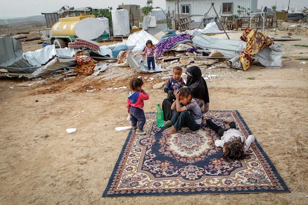 A Palestinian family sits in the remains of their demolished home in the West Bank village of Umm al-Kheir, April 6, 2016. (Wissam Hashlamon/Flash90)