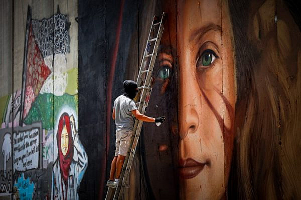 A man paints a mural of Palestinian Ahed Tamimi on a part of the West Bank separation wall in the West Bank city of Bethlehem, July 25, 2018. (Wisam Hashlamoun/Flash90)