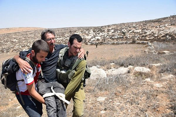 A Ta'ayush activist is carried away after being attacked by settlers in the illegal outpost of Mitzpe Yair, South Hebron Hills, August 25, 2018. (Nasser Nawaja/B'Tselem)