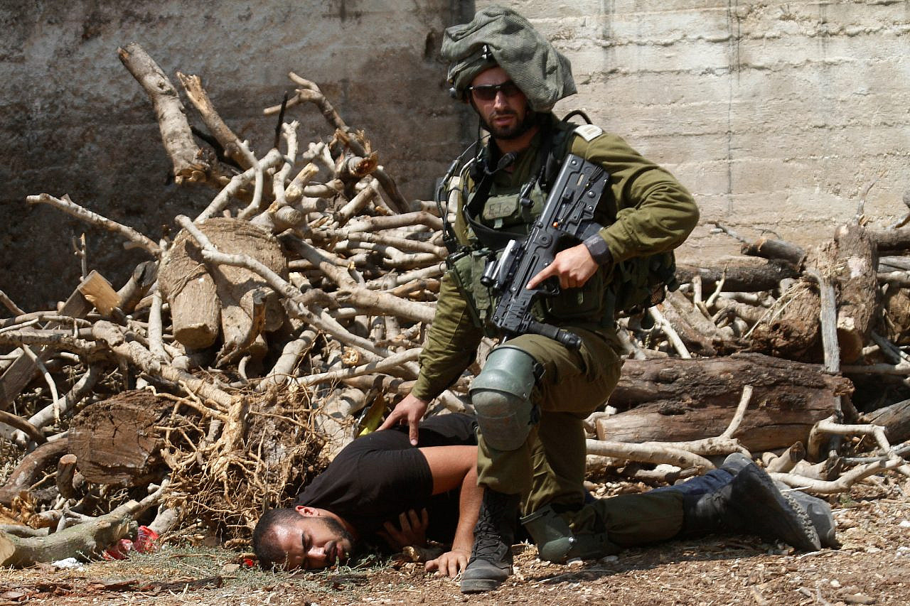 An Israeli soldier kneels over a Palestinian protester in the village of Kfar Qaddum, near Nablus, August 23, 2019. (Nasser Ishtayeh/Flash90)