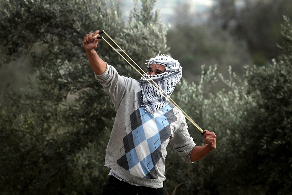 A Palestinian student from Birzeit University uses a slingshot to throw stones at Israeli troops during clashes with soldiers at the Atara checkpoint as they protest against Israel's military action on the Gaza Strip. November 19, 2012. (Issam Rimawi / FLASH90)