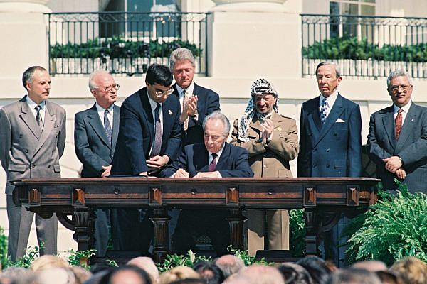 Israeli Foreign Minister Shimon Peres signs the Oslo Accords on the White House Lawn. Behind him are U.S. President Bill Clinton, PLO Chairman Yasser Arafat, Israeli Prime Minister Yitzhak Rabin, Palestinian Prime Minister Mahmoud Abbas and other world leaders, Washington DC, September 13, 1994. (Avi Ohayon/GPO)