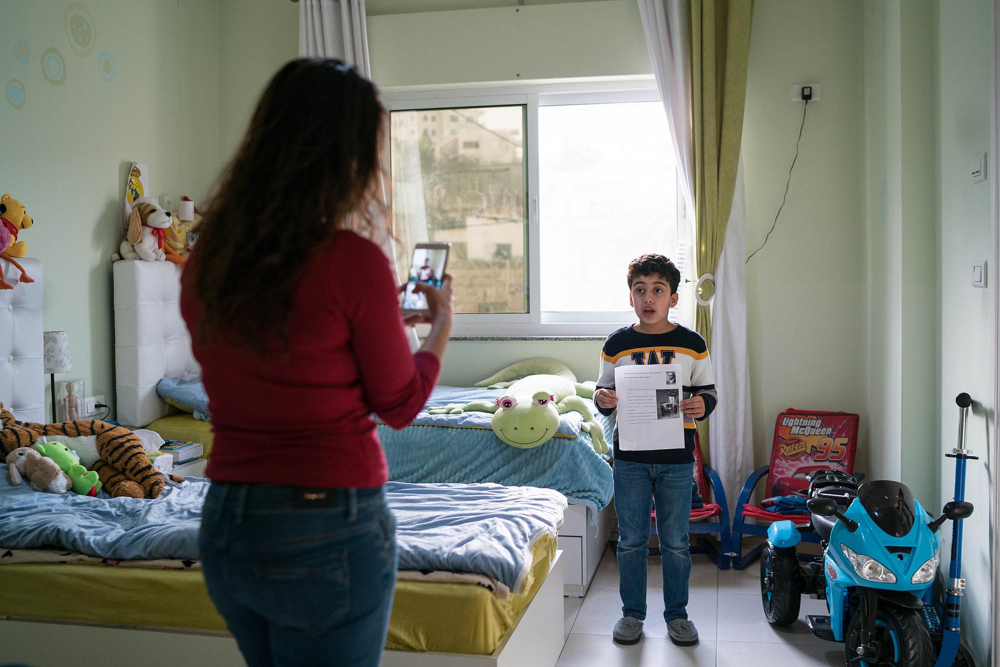 Carol Janine takes a video of her son Milan at their home in Bethlehem as he recites his homework, to send it to his teacher on March 11, 2020. (Samar Hazboun)