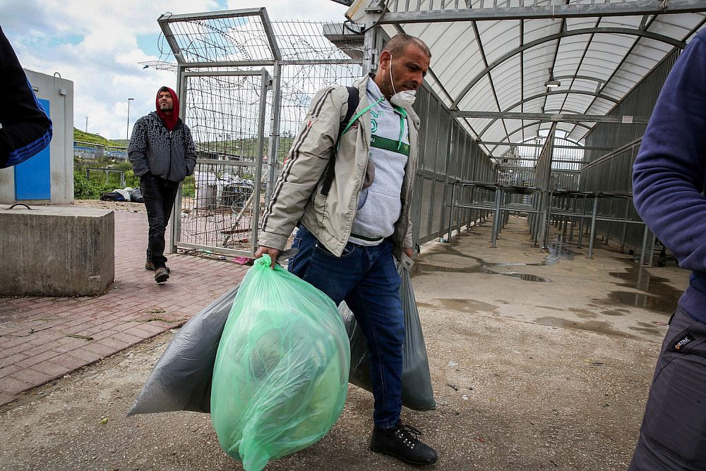 Palestinian workers from the West Bank city of Hebron carry personal belongings as they arrive to cross to Israel at a checkpoint in Tarqumiya, March 18, 2020. Photo by Wisam Hashlamoun/Flash90
