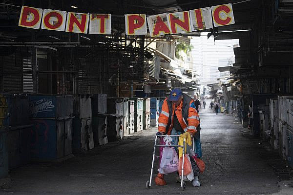 A homeless person walks past a banner that was put up by an art student at the closed Carmel Market in Tel Aviv, March 24, 2020. (Oren Ziv)