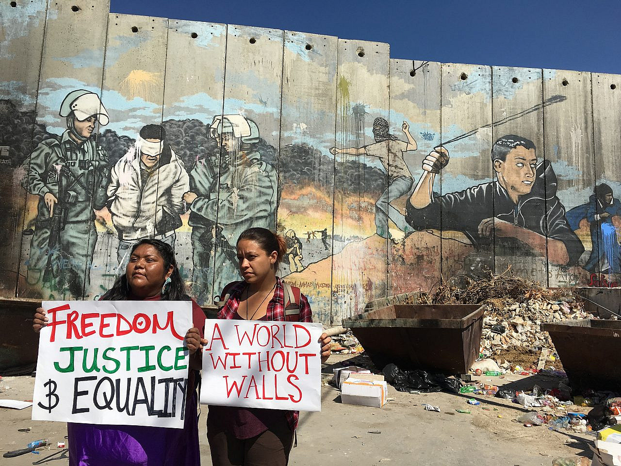 Activists with the U.S. Campaign for Palestinian Rights hold signs in front of Israel's separation wall in the West Bank. (Courtesy of USCPR)