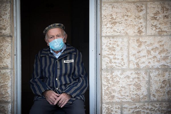 A Holocaust survivor is seen wearing a face mask as he sits at his porch in Jerusalem on Holocaust Remembrance Day, April 21, 2020. (Yonatan Sindel/Flash90)