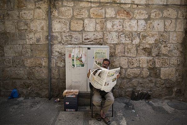 A Palestinian man reads the newspaper as he sits outside his souvenir shop in the souq, the market in Jerusalem's Old City. September 13, 2013. (Yonatan Sindel/Flash90.)
