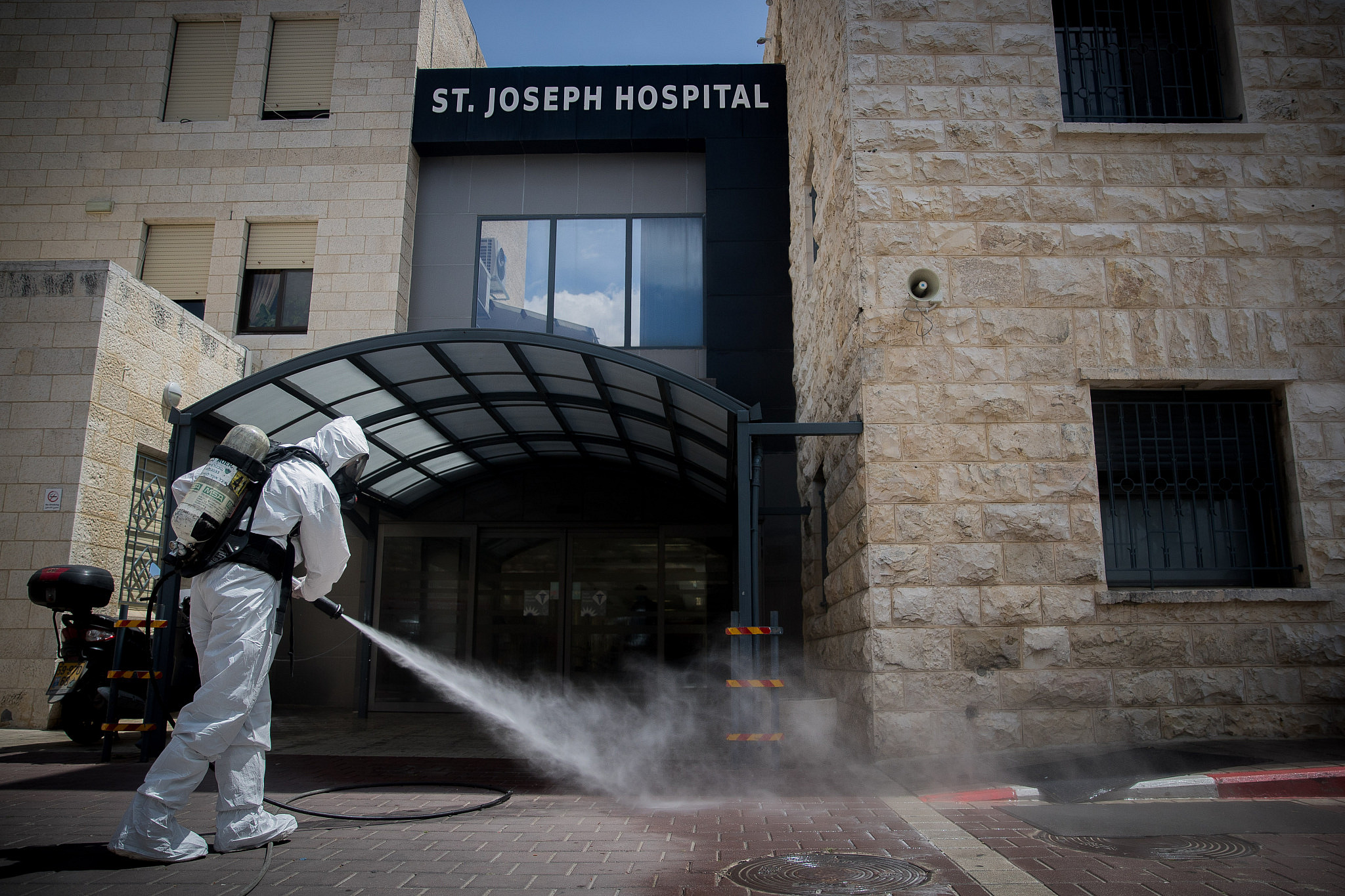 An Israeli firefighter disinfects the entrance to St Joseph Hospital in East Jerusalem as a preventive measure against the spread of the coronavirus, April 16, 2020, (Yonatan Sindel/Flash90)