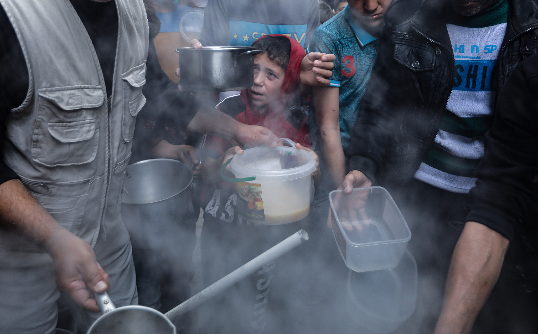Residents of the Shuja'iyya neighborhood in Gaza huddle around Walid Hattab's cauldron of soup for iftar, April 25, 2020. (Mohammed Zaanoun)