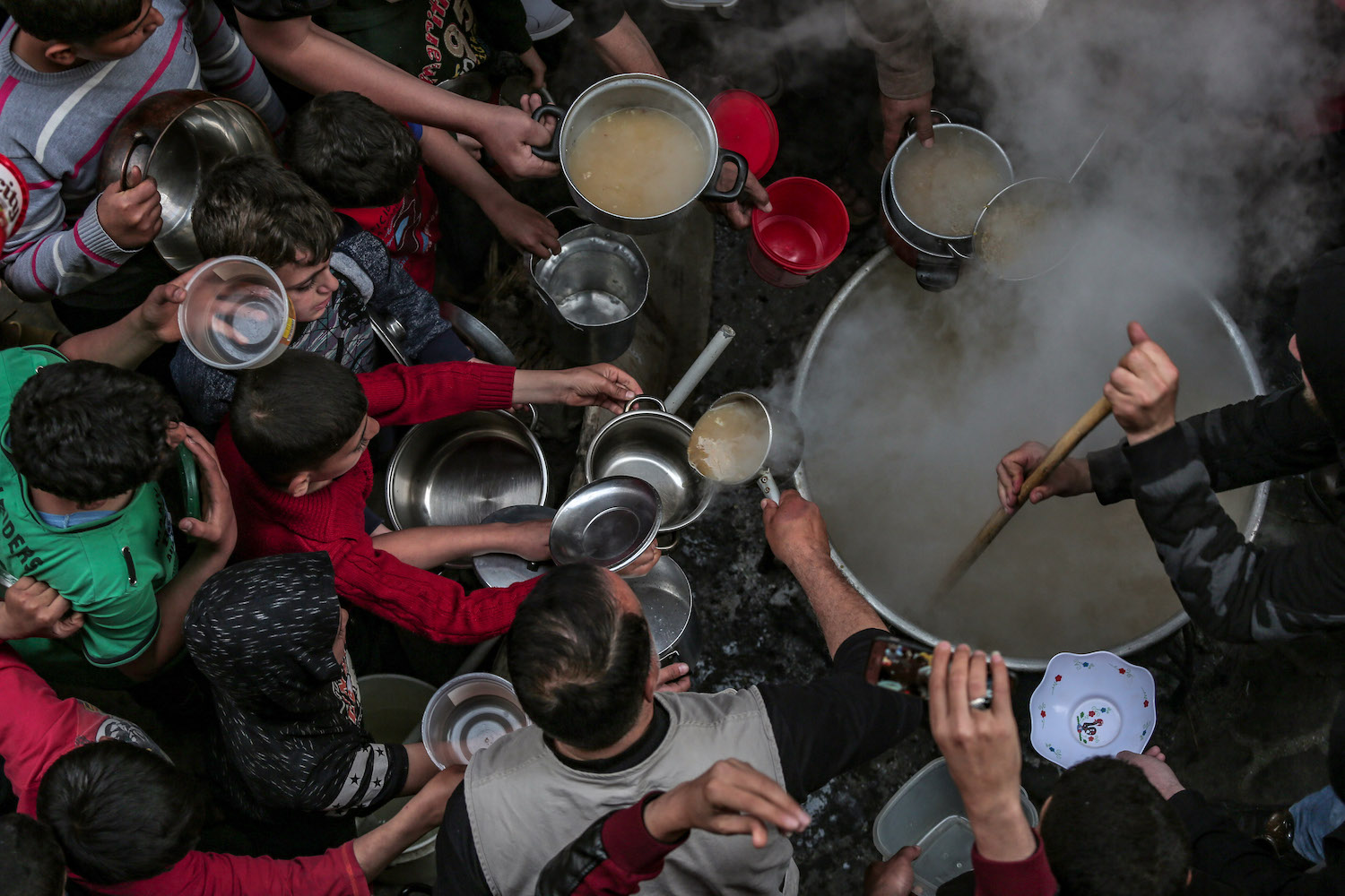 Residents of the Shuja'iyya neighborhood in Gaza huddle around Walid Hattab's cauldron of soup for iftar, April 25, 2020. (Mohammed Zaanoun)