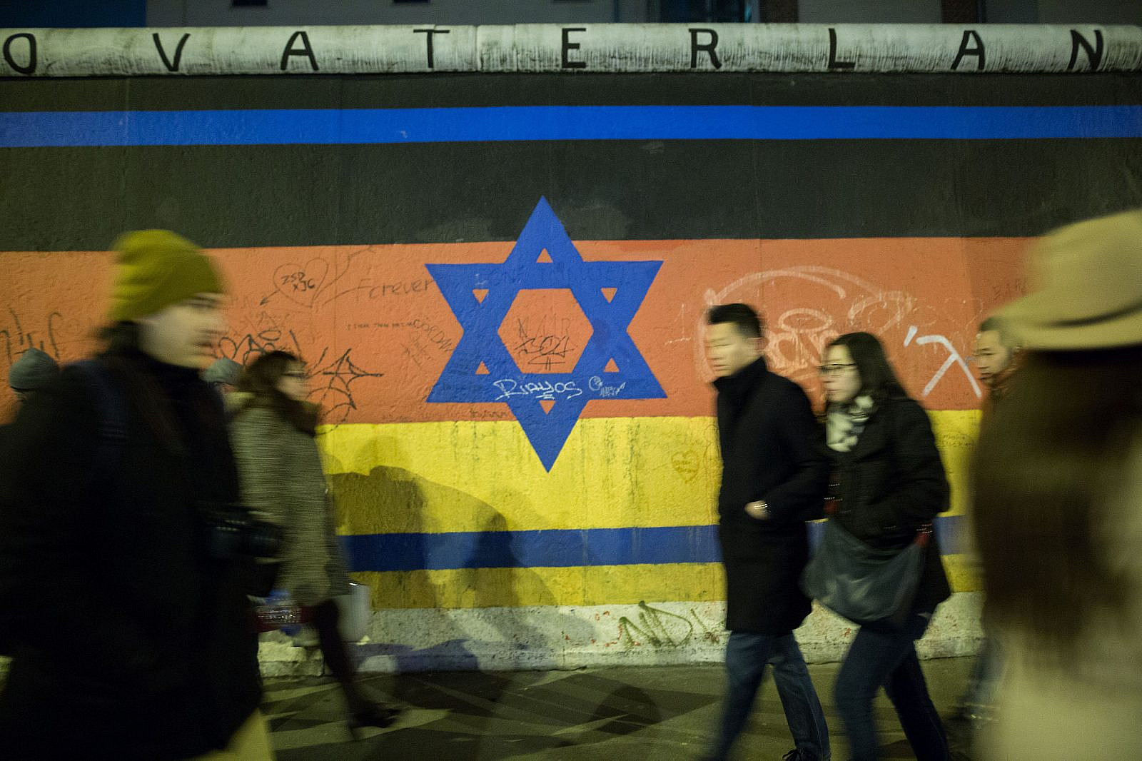 People walk by a mural depicting a combination of the Israeli and German flag on the Berlin wall. March 13, 2016. (Noam Revkin Fenton/FLASH90)