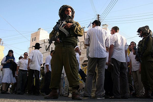 Israeli soldiers guard Jewish settlers as they walk around the Palestinian market in the old town of Hebron in the West Bank on September 4, 2010. (Najeh Hashlamoun /Flash90)